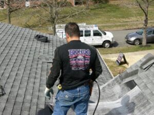 Roofer on steep shingled roof wearing logo