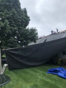 Roofers removing shingles under protective tarp