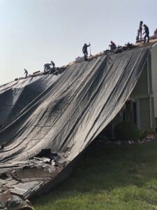 Roof tear-off with workers and debris tarp