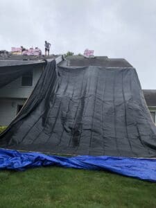 Roofers installing shingles under large tarp