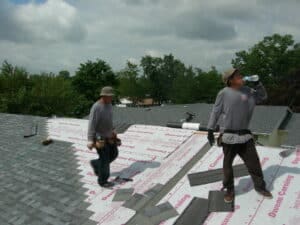 Workers installing shingles on home roof