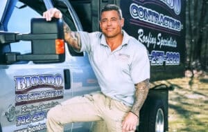 Worker leaning on branded roofing truck