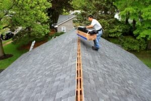 Roofer installing ridge vent on gray shingle roof
