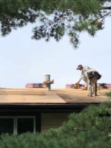 Roofer replacing shingles beside roof vent
