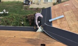 Worker installs roofing material on a sloped roof under sunny conditions.
